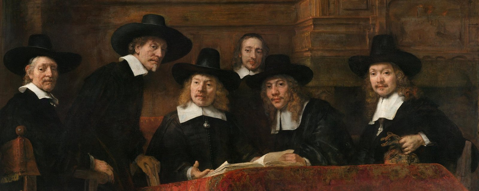 Rembrandt’s group portrait of six men in black hats and white collars around a table draped in a red Persian rug, an open sample book in front of them, looking up as if interrupted mid-decision